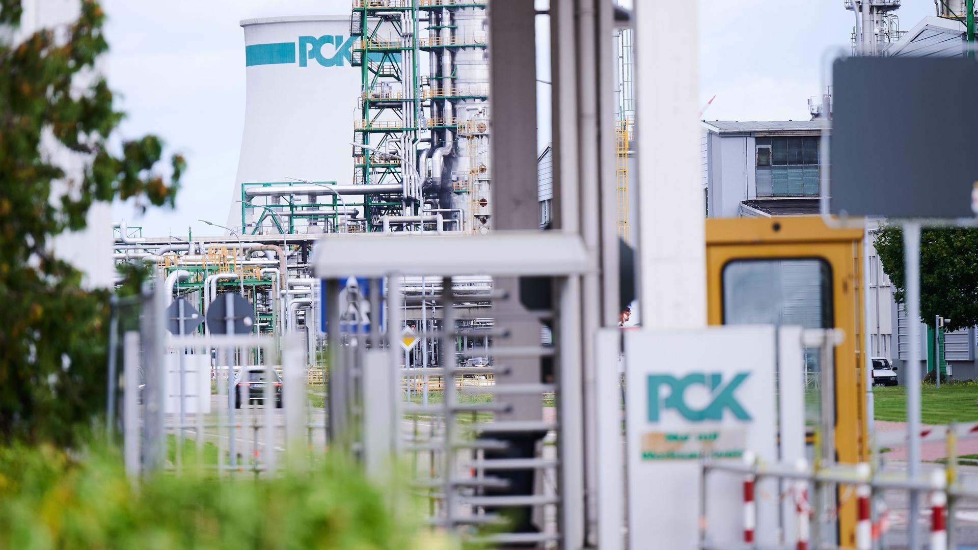 Das Bild zeigt das Werksgelände der Raffinerie PCK in Schwedt. Das Logo PCK ist im Vordergrund am Eingang zu sehen und im Hintergrund an einem Tank.