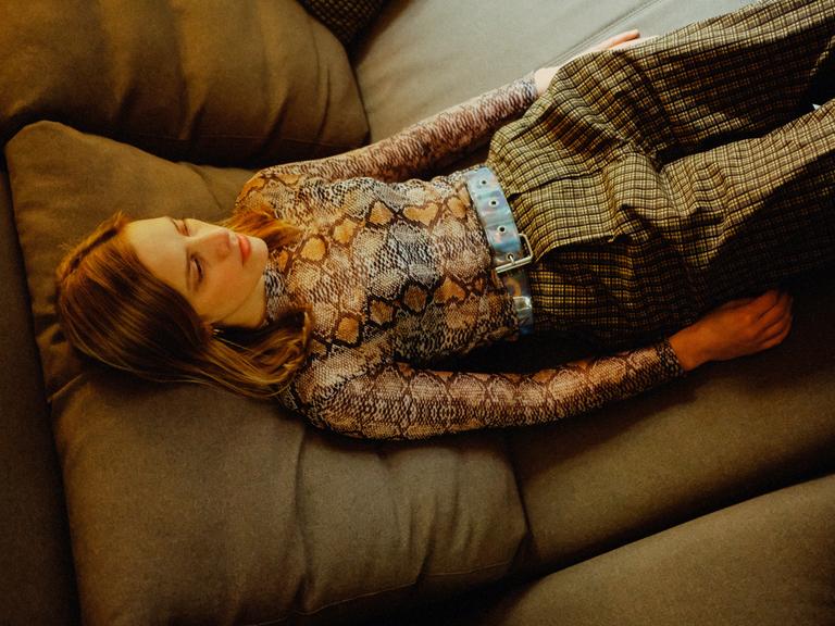 Eine junge Frau liegt auf einem breiten Sofa mit offenen Augen.