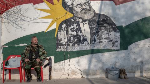 Ein kurdischer Soldat, Mitglied der Organisation für den Kampf des iranischen Kurdistans (Sazmani Khabat), sitzt auf einem Plastikstuhl vor einer Wand mit einem kurdischen Graffitti in der autonomen kurdischen Region im Norden des Irak. Ein kurdischer Soldat, Mitglied der Organisation für den Kampf des iranischen Kurdistans (Sazmani Khabat), sitzt auf einem Plastikstuhl vor einer Wand mit einem kurdischen Graffitti in der autonomen kurdischen Region im Norden des Irak.