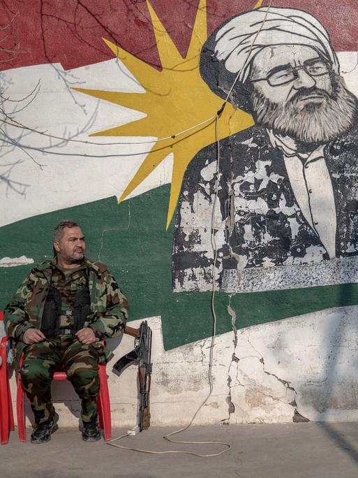 Ein kurdischer Soldat, Mitglied der Organisation für den Kampf des iranischen Kurdistans (Sazmani Khabat), sitzt auf einem Plastikstuhl vor einer Wand mit einem kurdischen Graffitti in der autonomen kurdischen Region im Norden des Irak.