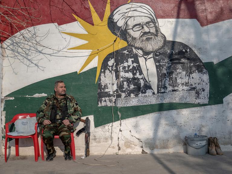 Ein kurdischer Soldat, Mitglied der Organisation für den Kampf des iranischen Kurdistans (Sazmani Khabat), sitzt auf einem Plastikstuhl vor einer Wand mit einem kurdischen Graffitti in der autonomen kurdischen Region im Norden des Irak.