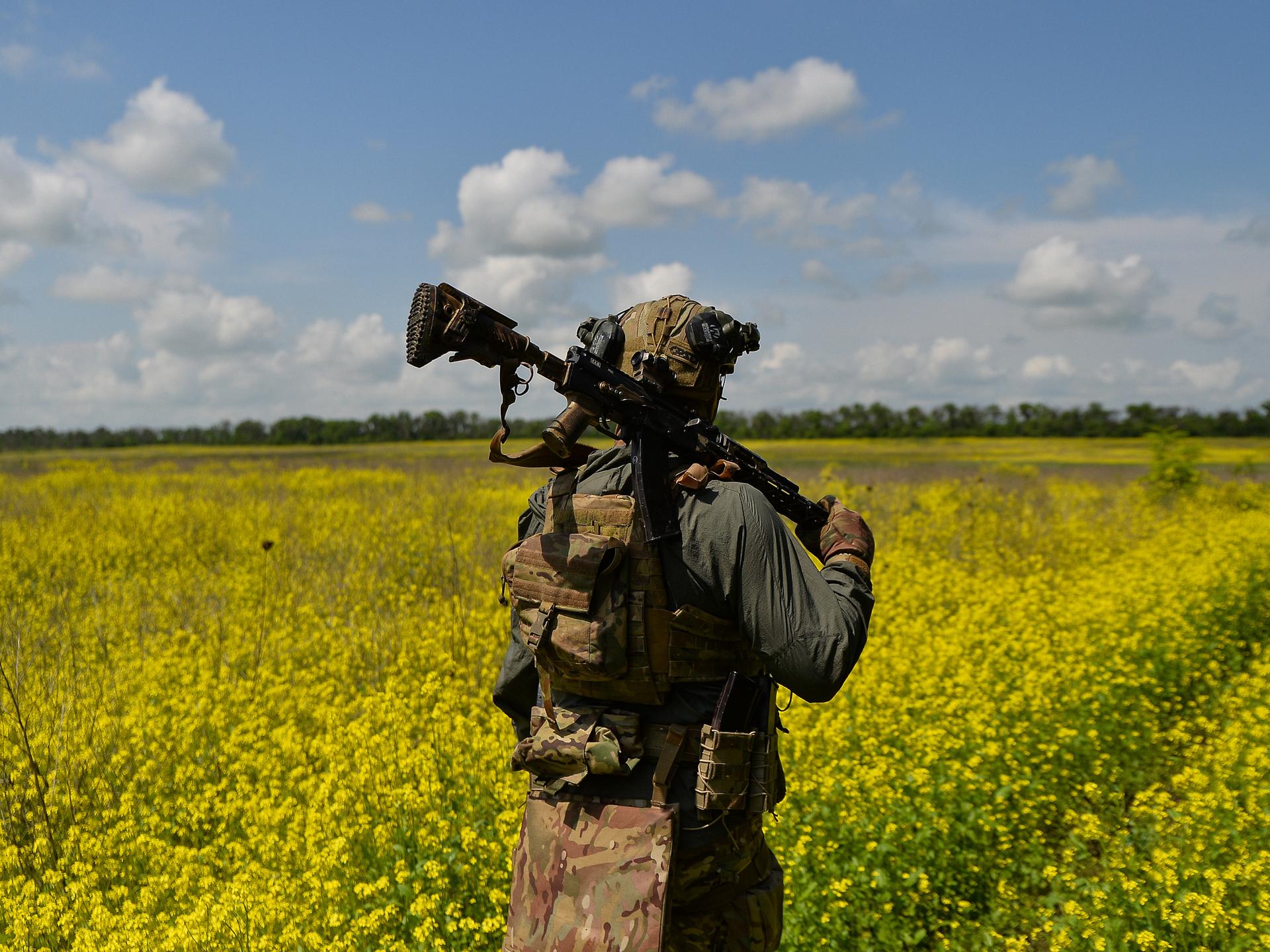 Ein ukrainischer Soldat läuft mit der Waffe über der Schulter durch ein blühendes Feld. 