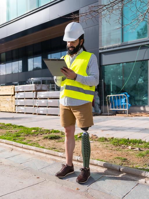 Ingenieur mit Beinprothese arbeitet mit Schutzausrüstung auf einer Baustelle 