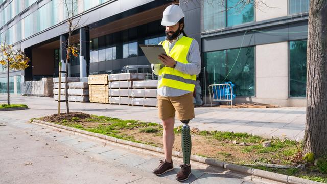 Ingenieur mit Beinprothese arbeitet mit Schutzausrüstung auf einer Baustelle 