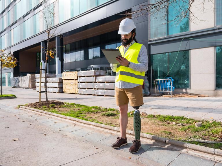 Ingenieur mit Beinprothese arbeitet mit Schutzausrüstung auf einer Baustelle 