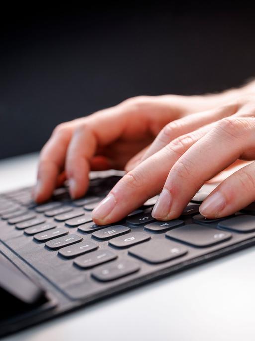 Hände tippen auf einem Tablet mit Tastatur