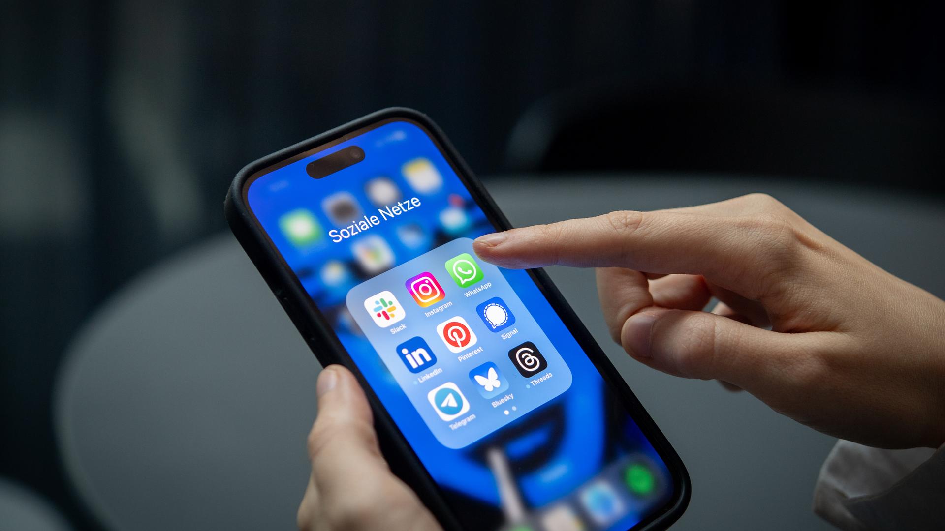 Ein Finger tipps auf ein Smartphone. Darauf sieht man verschiedene Apps, zum Beispiel den Messenger-Dienst Signal.