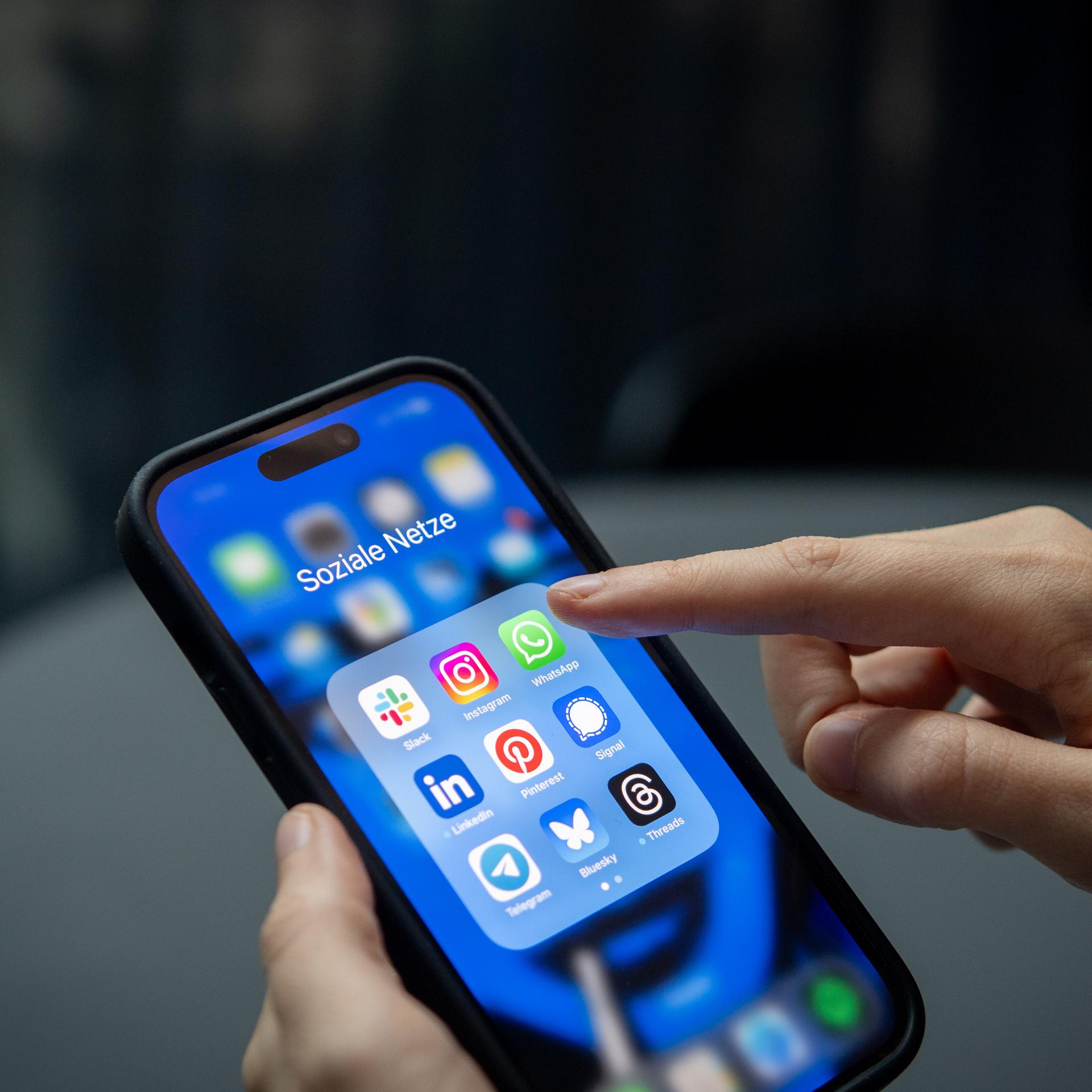 Ein Finger tipps auf ein Smartphone. Darauf sieht man verschiedene Apps, zum Beispiel den Messenger-Dienst Signal.