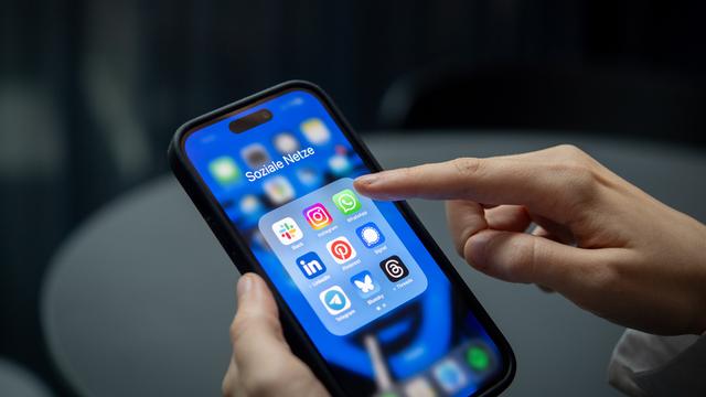 Ein Finger tipps auf ein Smartphone. Darauf sieht man verschiedene Apps, zum Beispiel den Messenger-Dienst Signal.