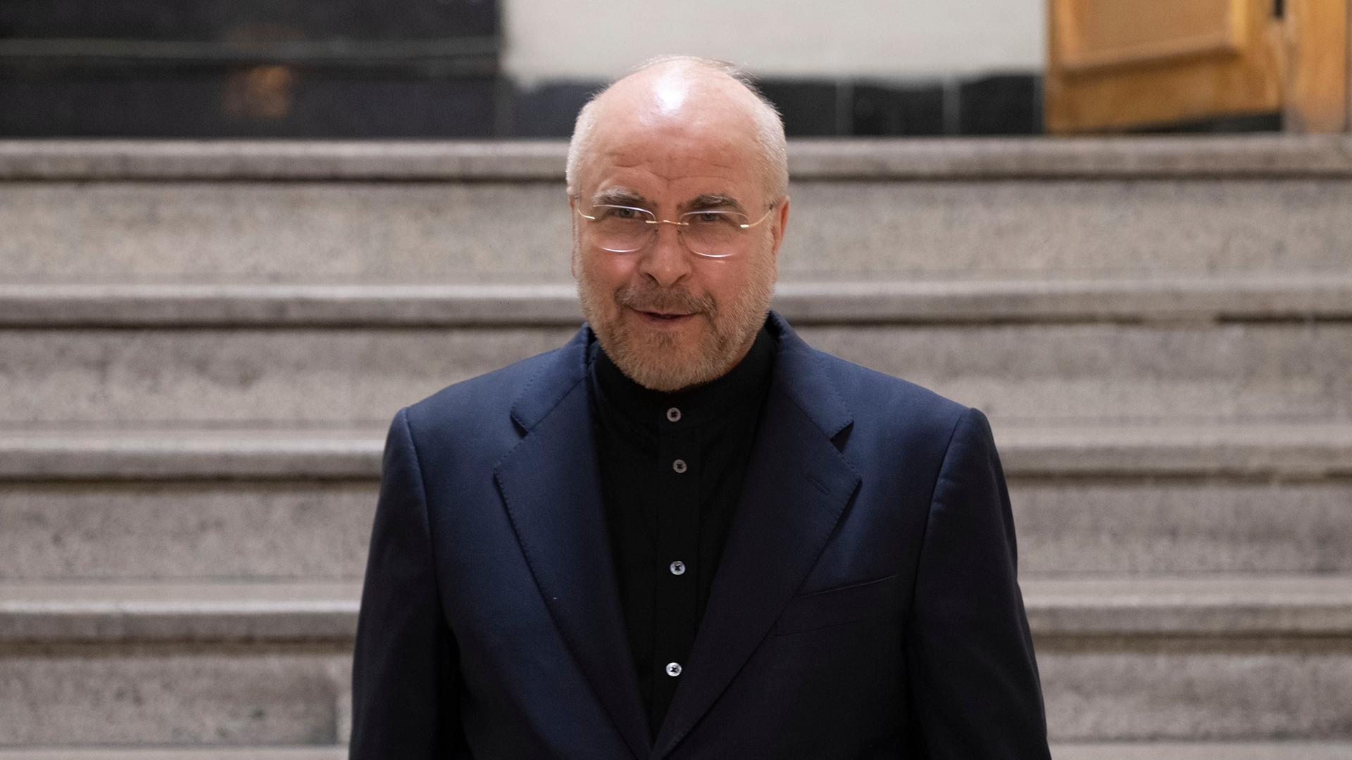 Man sieht einen Mann mit wenigen kurzen grauen Haaren, einem kurzen Bart und Brille. Er trägt ein dunkelblaues Hemd und ein dunkles Sacko. Man sieht einen Mann mit wenigen kurzen grauen Haaren, einem kurzen Bart und Brille. Er trägt ein dunkelblaues Hemd und ein dunkles Sacko.