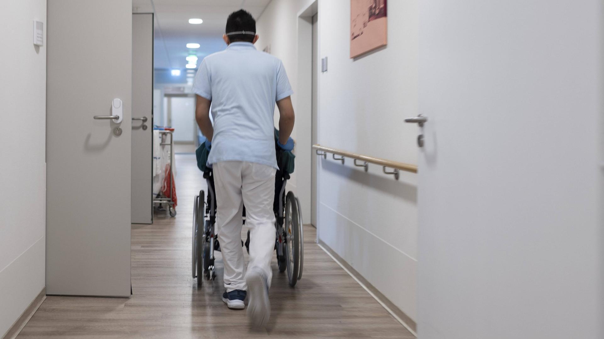 Eine Pflegekraft schiebt einen Rollstuhl durch einen Gang 