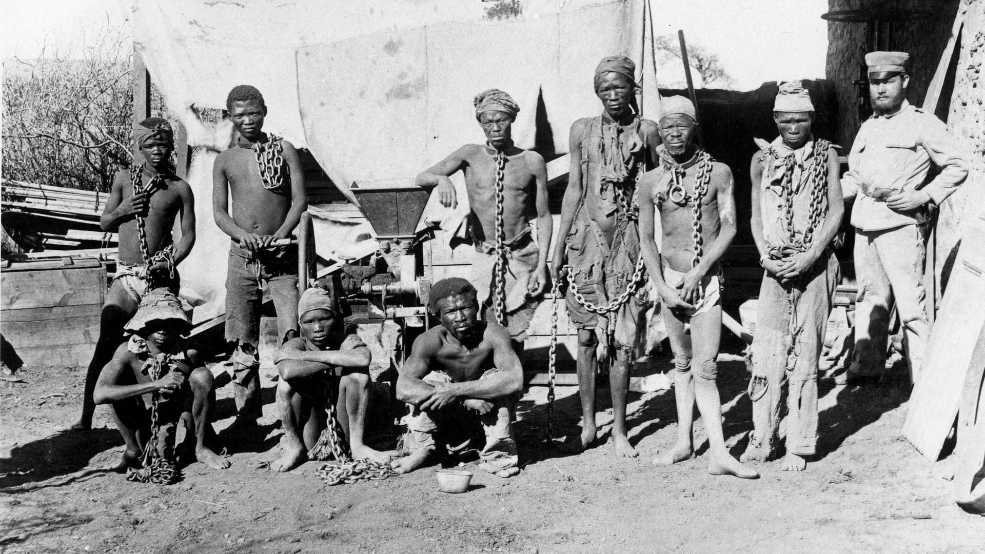 Herero- und Nama-Gefangene um 1904 im damaligen Deutsch-Südwestafrika (heute Namibia). Sie sind angekettet und werden von einem deutschen Soldaten bewacht. Herero- und Nama-Gefangene um 1904 im damaligen Deutsch-Südwestafrika (heute Namibia). Sie sind angekettet und werden von einem deutschen Soldaten bewacht.