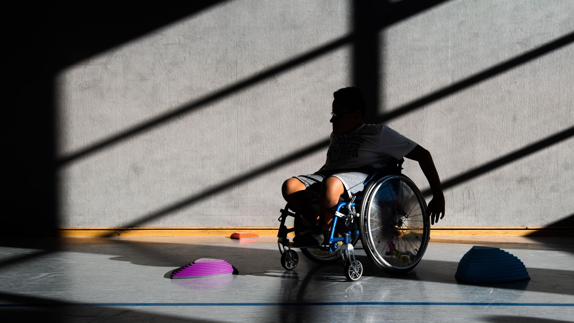 Ein Schüler einer Förderschule fährt in der Sporthalle des Gymnasium Burgdorf mit seinem Rollstuhl Slalom um Hindernisse. 