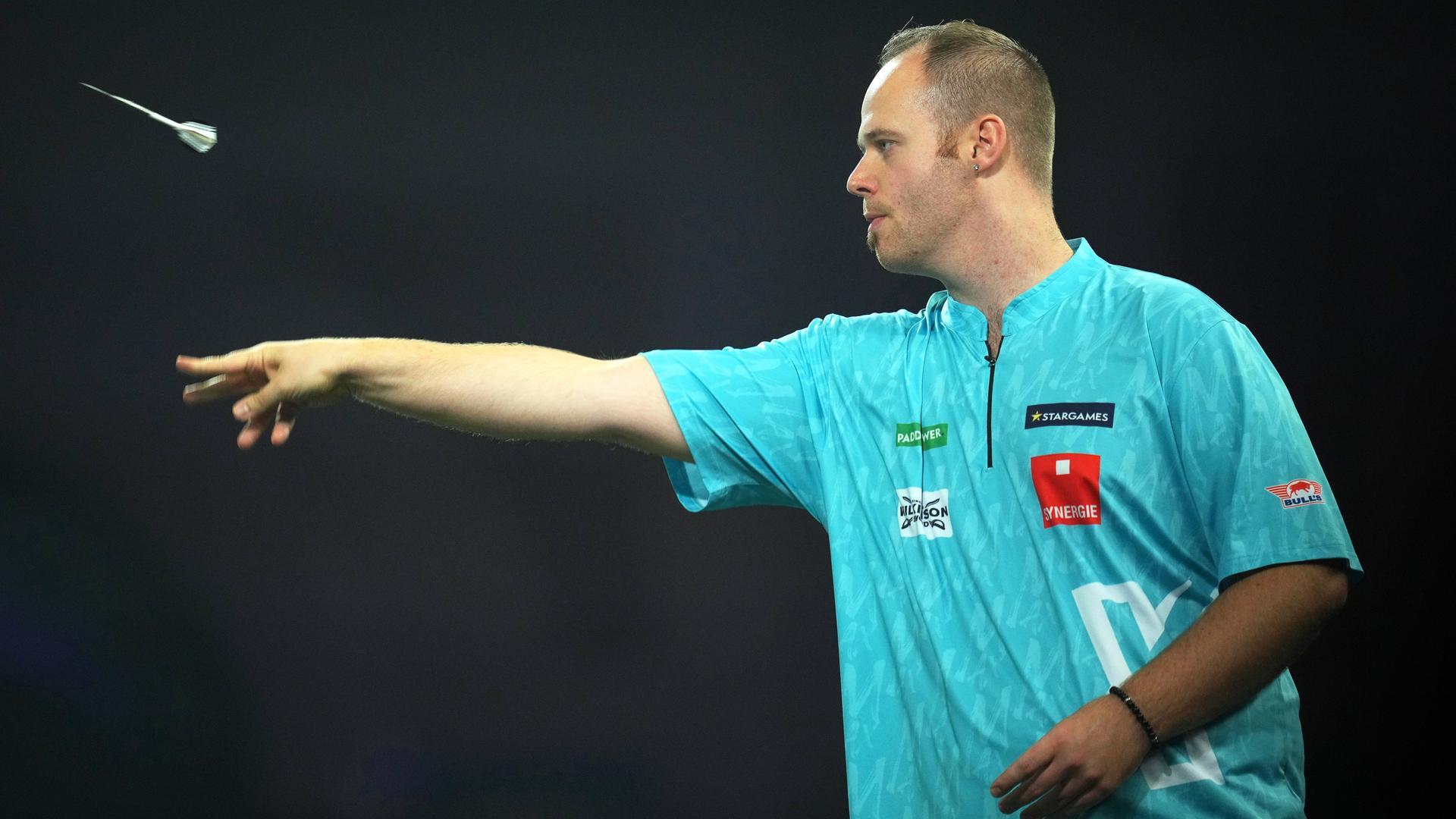 Das Bild zeigt den deutschen Dart-Spieler Max Hopp von der Seite. Er trägt ein türkisfarbenes Trikot und wirft einen Dart-Pfeil in Richtung Zielscheibe.