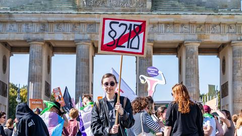 Eine junge Demonstrantin hält während eines Protest vor dem Brandenburger Tor ein Schild mit der durchgestrichenen Aufschrift "§ 218" in die Höhe.