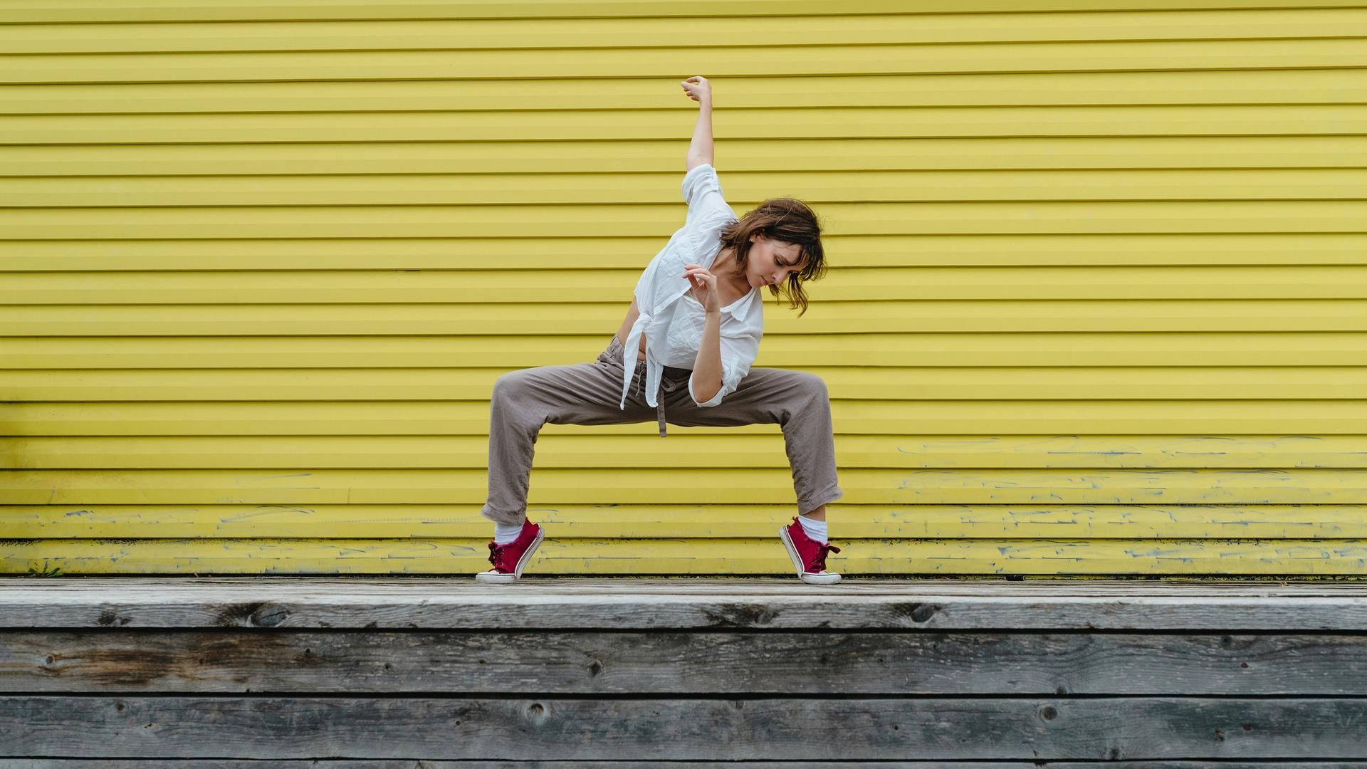 Junge Frau tanzt einen Breakdancemove auf einem Bürgersteig.