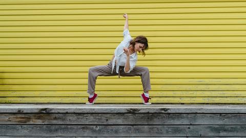 Junge Frau tanzt einen Breakdancemove auf einem Bürgersteig.