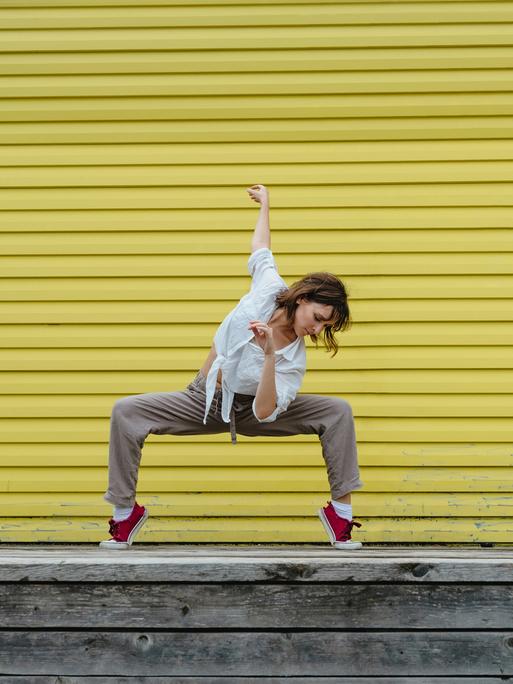 Junge Frau tanzt einen Breakdancemove auf einem Bürgersteig.