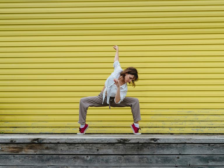 Junge Frau tanzt einen Breakdancemove auf einem Bürgersteig.