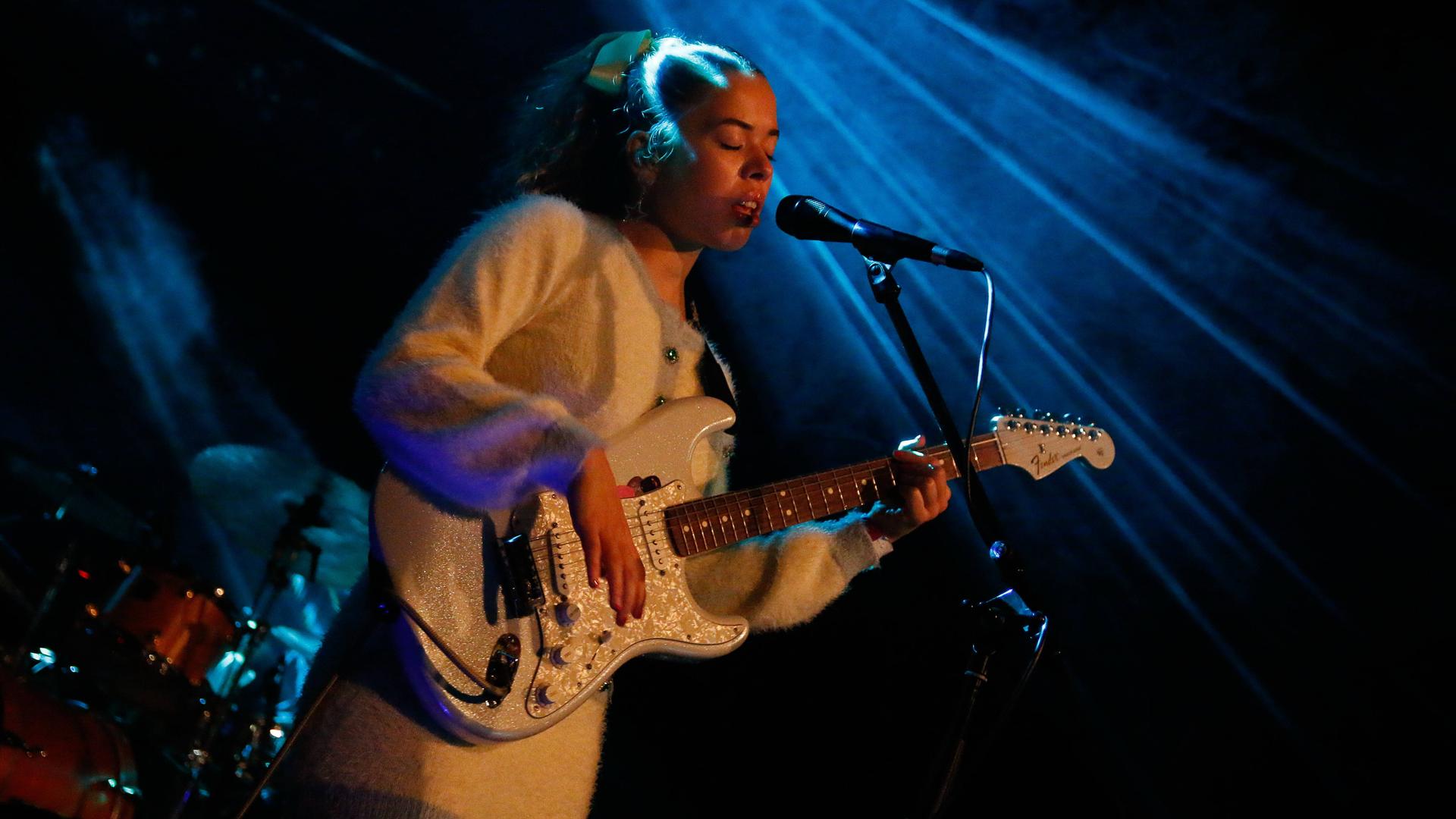 Die Musikerin Nilüfer Yanya ist ganz in weiß gekleidet und spielt auch eine weiße Gitarre. Die Musikerin Nilüfer Yanya ist ganz in weiß gekleidet und spielt auch eine weiße Gitarre.