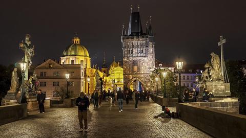 Die Karlsbrücke in Prag bei Nacht, viele Menschen sind unterwegs, einige schauen auf das Display ihres Mobiltelefons.