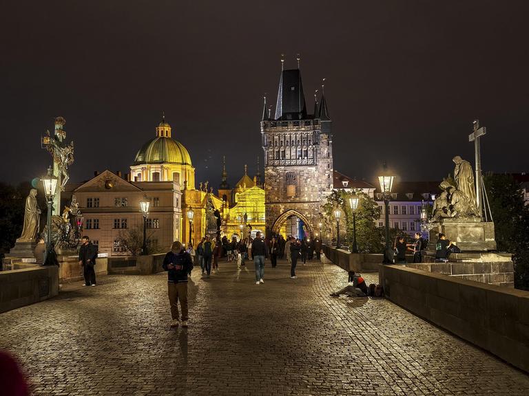 Die Karlsbrücke in Prag bei Nacht, viele Menschen sind unterwegs, einige schauen auf das Display ihres Mobiltelefons.