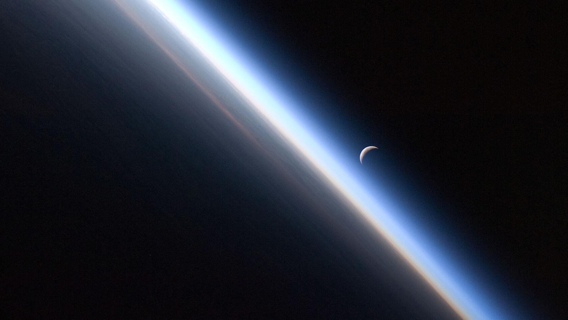 Blick auf die Erdatmosphäre (mit der Mondsichel im Hintergrund), aufgenommen von Bord der ISS. 