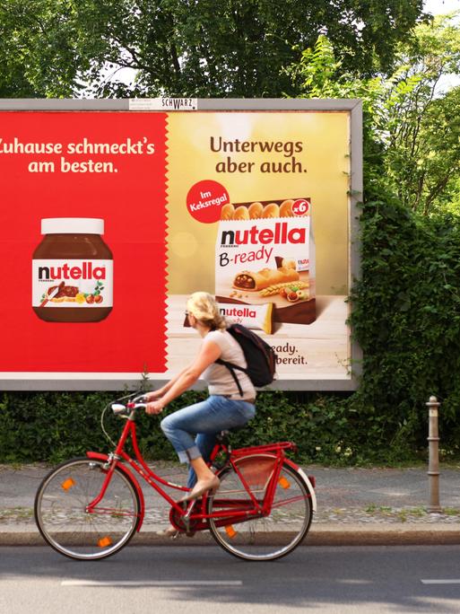 Eine Frau fährt mit dem Fahrrad an einem Plakat mit Webung für Nutella und Nutella B-ready von Ferrero vorbei.