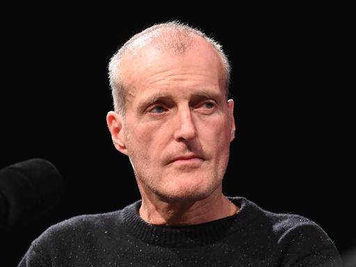 Robert Seethaler, in einem dunklen Pullover und vor schwarzem Bühnenhintergrund, nimmt an einem Podiumsgespräch teil.