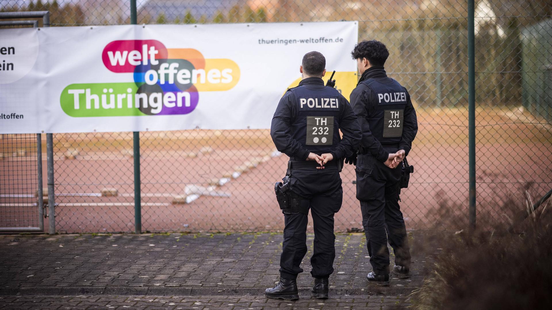 Polizisten stehen vor einem Zaun Wache, an dem auf einem Plakat geschrieben steht: "weltoffenes Thüringen".