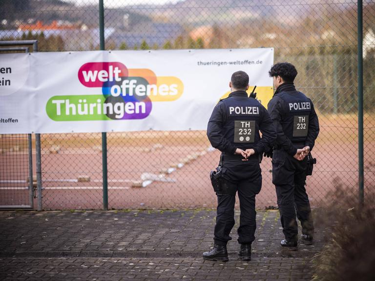 Polizisten stehen vor einem Zaun Wache, an dem auf einem Plakat geschrieben steht: "weltoffenes Thüringen".