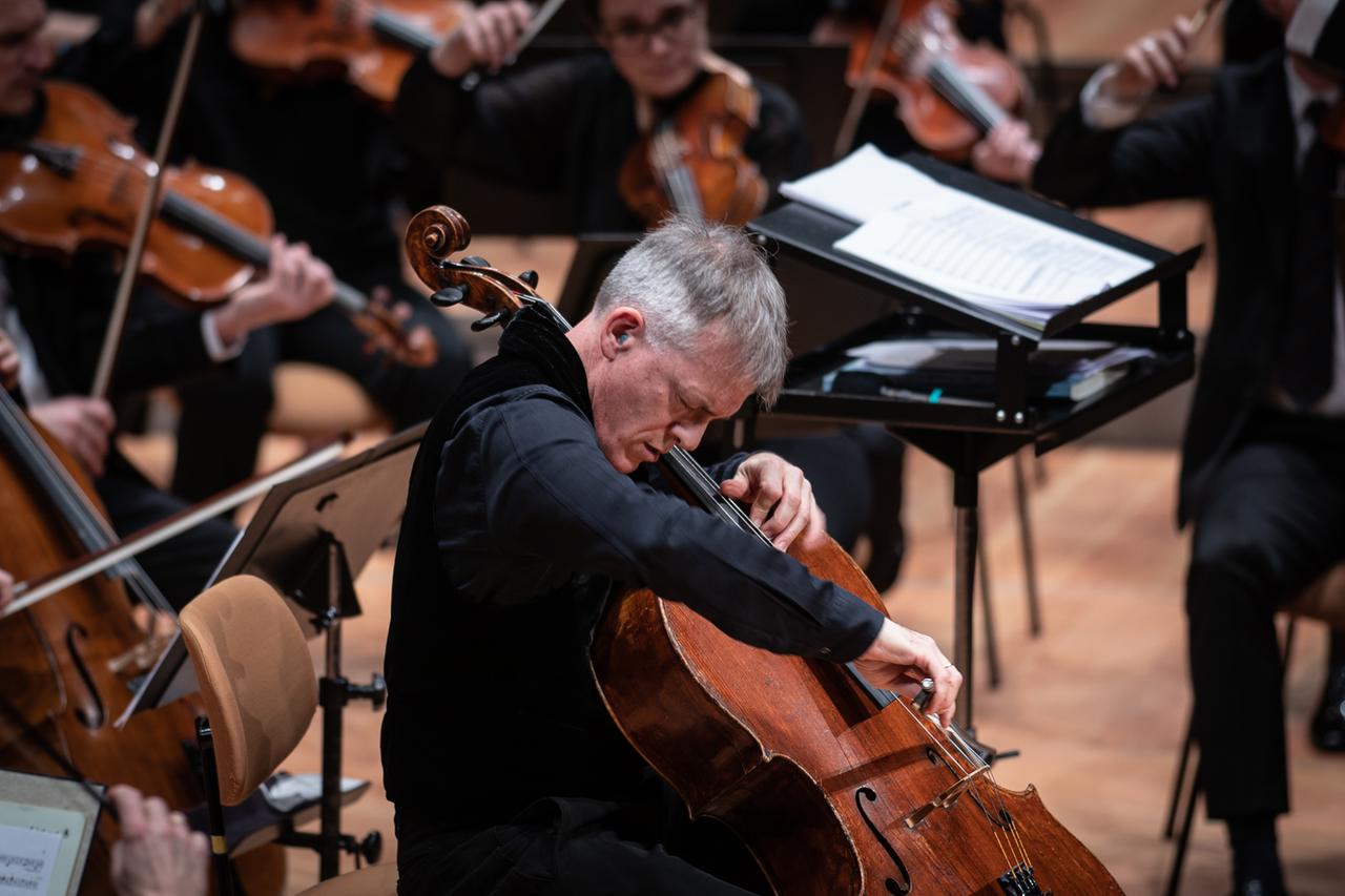 Alban Gerhardt sitzt vertieft ins Cellospiel vor Musikern des Rundfunk-Sinfonierorchesters Berlin.