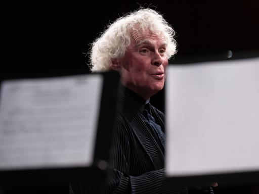 Blick durch Notenpulte hindurch, hinter denen Sir Simon Rattle steht.