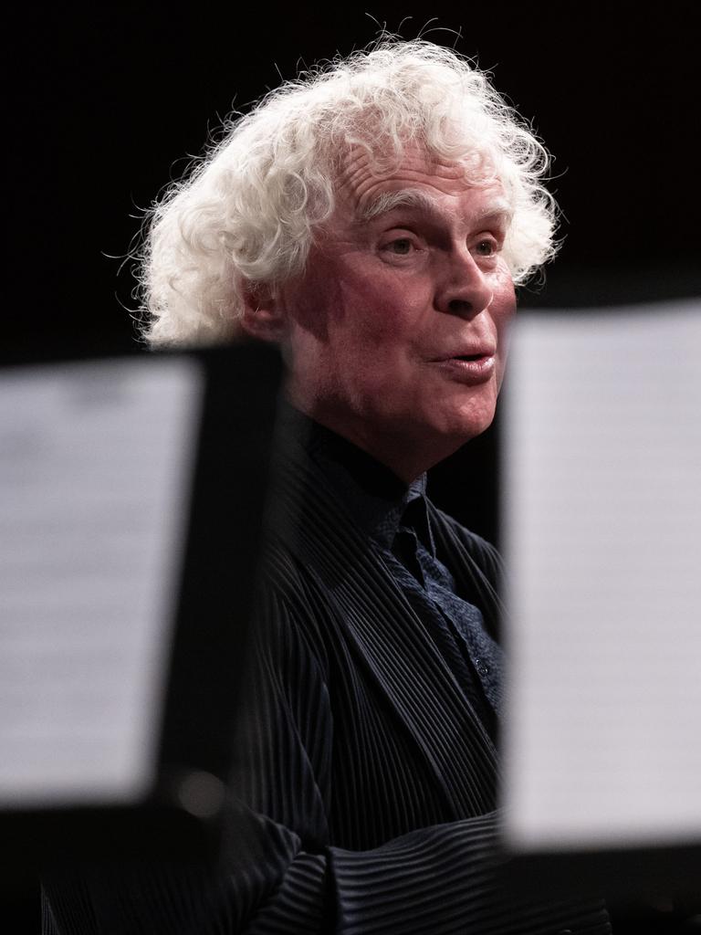 Blick durch Notenpulte hindurch, hinter denen Sir Simon Rattle steht.