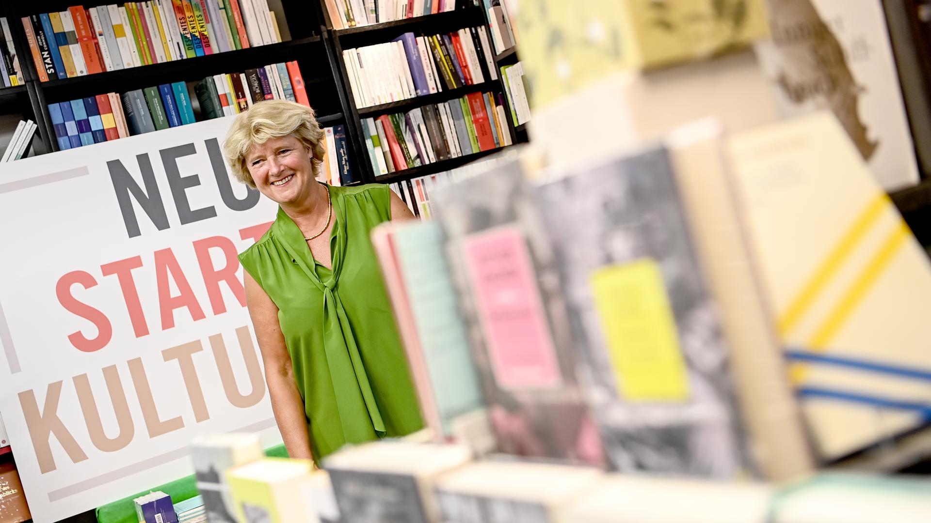 Kulturstaatsministerin Monika Grütters steht inmitten vieler Bücher in einer Buchhandlung, neben ihr ein Schild mit der Aufschrift "Neustart Kultur".