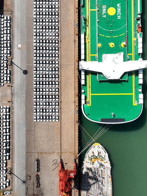 E-Autos am Hafen von Lianyungang in China neben einem Frachtschiff