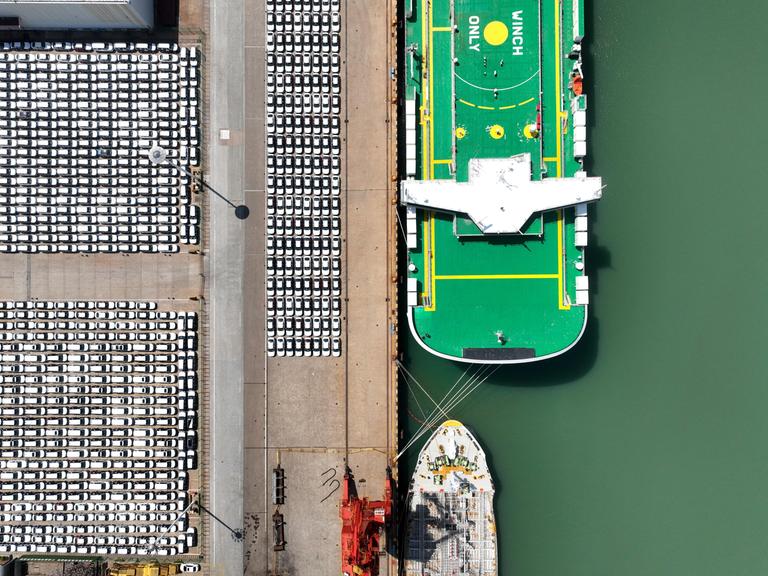 E-Autos am Hafen von Lianyungang in China neben einem Frachtschiff