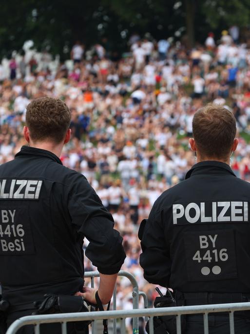 Zwei Polizisten blicken aus einiger Entfernung auf die Zuschauer in der Fanzone im Münchner Olympiapark.