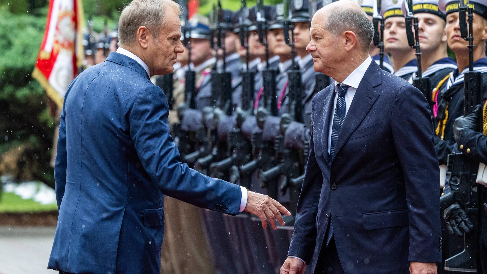 Premierminister Donald Tusk (links) empfängt Bundeskanzler Olaf Scholz (rechts). Sie sprechen miteinander während einer Militärparade.