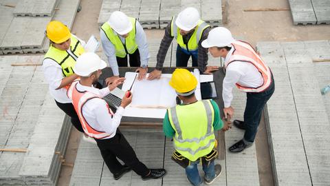 Auf einer Baustelle stehen Handwerker und Ingenieure zusammen und tragen gelbe und weiße Helme auf den Köpfen.