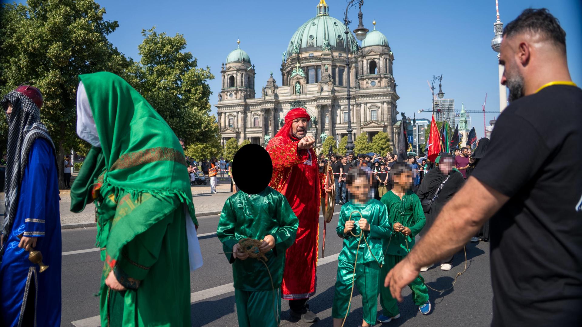 Kinder in langen grünen Gewändern werden an einem Seil über die Straße am Berlin Dom geführt. 