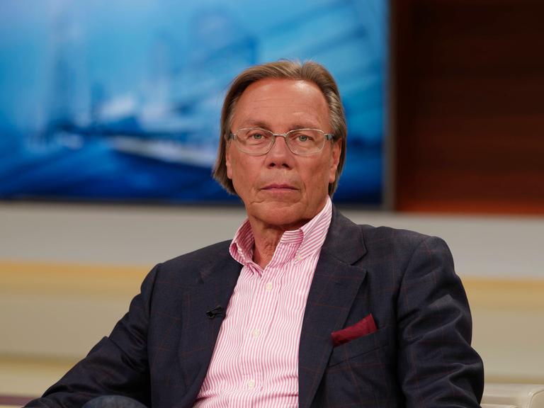 Der Soziologe Harald Welzer sitzt in einem Fernsehstudio. Er trägt ein rosa-gestreiftes Hemd, im Hintergrund ist unscharf ein Fernseher erkennbar.  