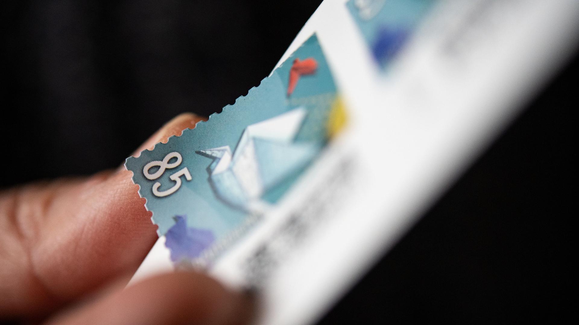 Eine Frau löst eine 85 Cent Briefmarke von einem Bogen.