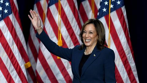 Wisconsin, USA: Vize Präsidentin Kamala Harris hält eine Rede während ihrer Kampagne in einer High School. Sie steht vor mehreren US-Flaggen und winkt mit der rechten Hand.