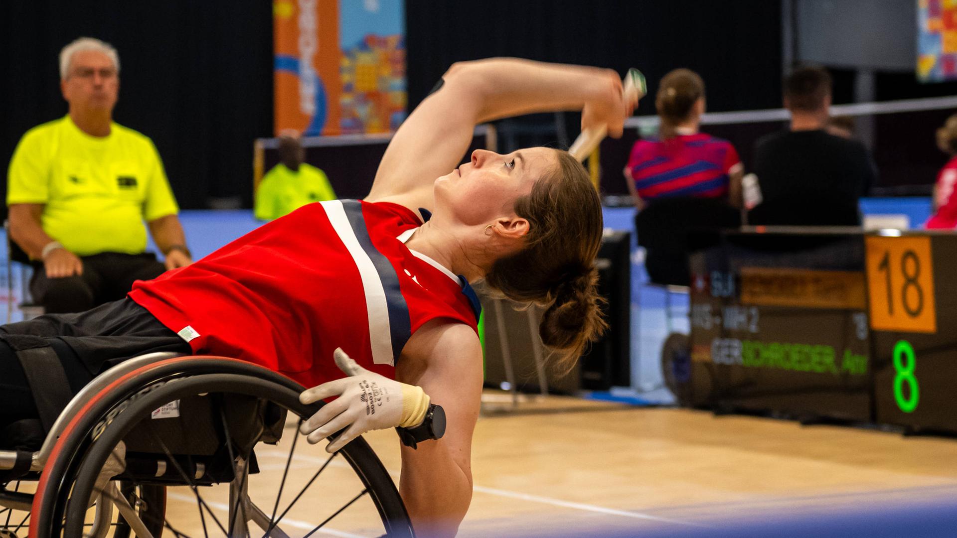 Die Badminton-Para-Athletin Annika Schröder beugt sich in ihrem Rollstuhl weit nach hinten, um den Federball anzunehmen.