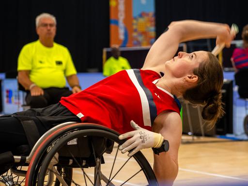 Die Badminton-Para-Athletin Annika Schröder beugt sich in ihrem Rollstuhl weit nach hinten, um den Federball anzunehmen.