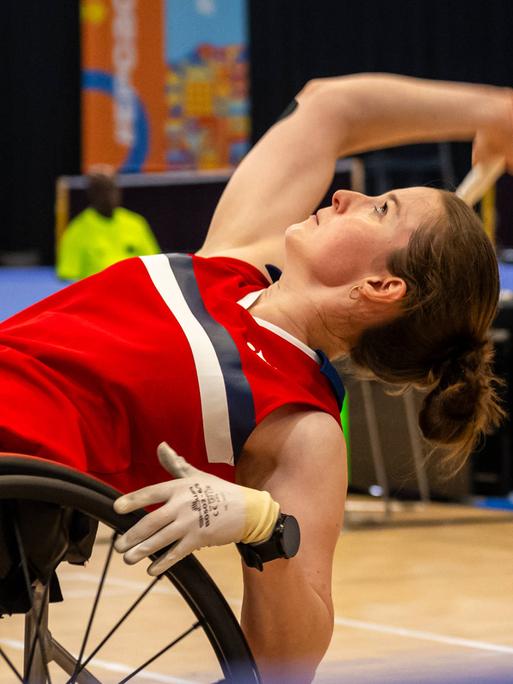 Die Badminton-Para-Athletin Annika Schröder beugt sich in ihrem Rollstuhl weit nach hinten, um den Federball anzunehmen.