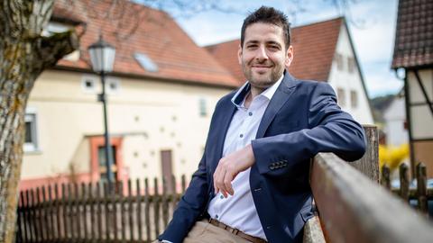 Ryyan Alshebl sitzt im Anzug in Ostelsheim auf einer Parkbank und lächelt in die Kamera.