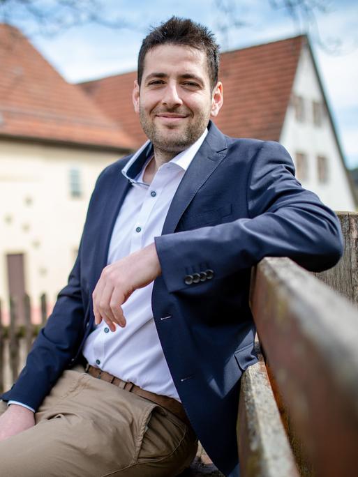 Ryyan Alshebl sitzt im Anzug in Ostelsheim auf einer Parkbank und lächelt in die Kamera.