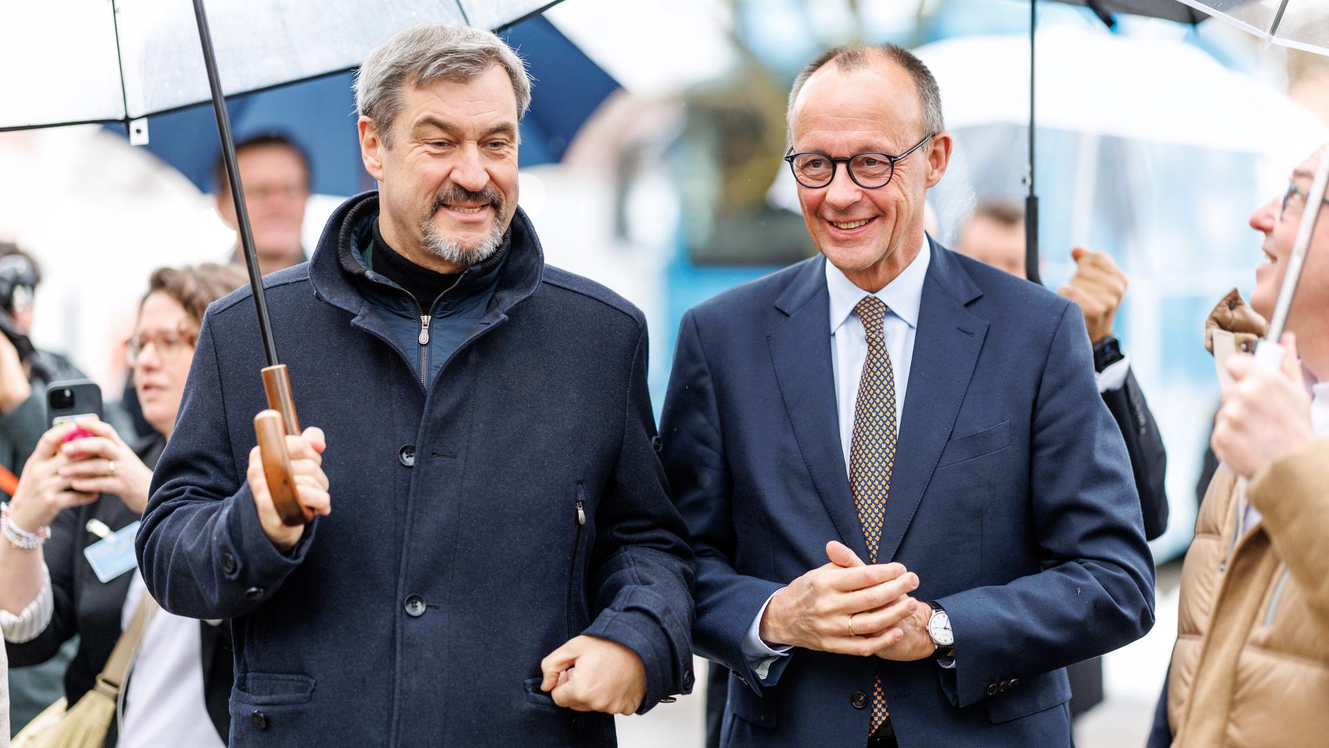 Markus Söder (CSU), Parteivorsitzender und Ministerpräsident von Bayern, und Friedrich Merz, Bundesvorsitzender der CDU und CDU-Kanzlerkandidat stehen nebeneinander unter Schirmen.